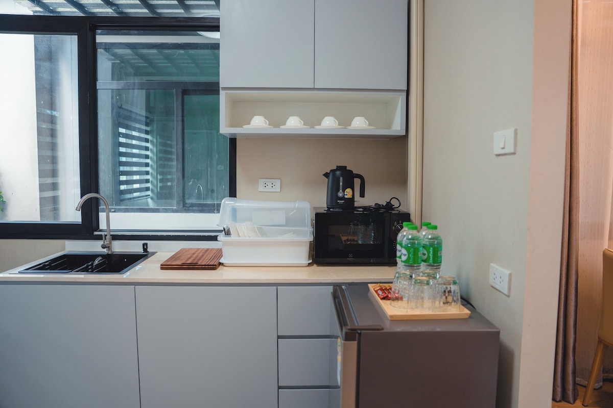 Eine kompakte Küche mit Spüle, Kaffeemaschine, Mikrowelle und kleinem Kühlschrank.