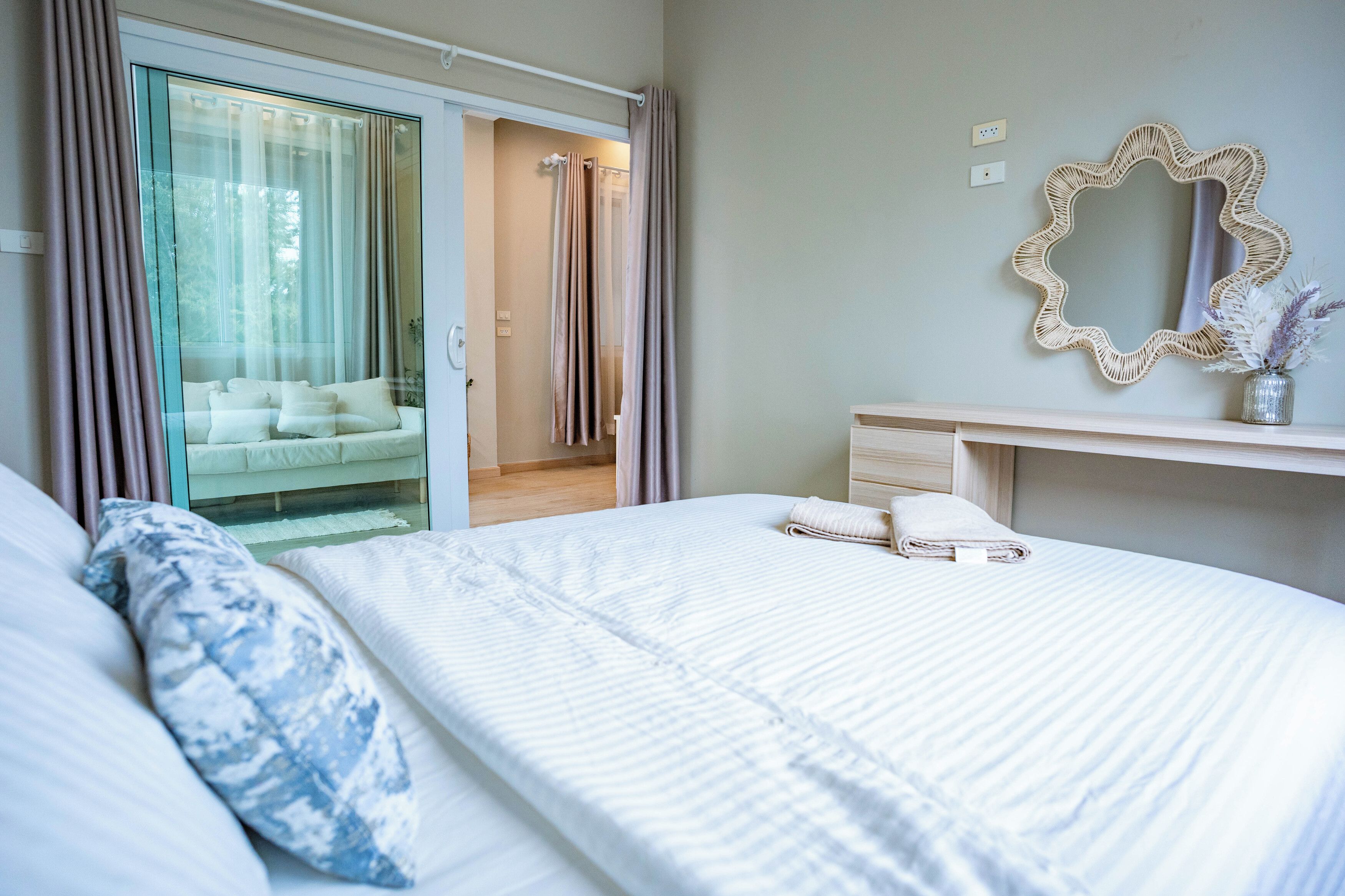A bedroom with a bed, a bedside table, a mirror, and a sliding glass door leading to a balcony.