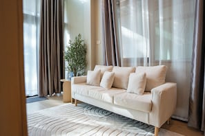 A modern living room with a beige sofa, a patterned rug, and sheer curtains. - Sea House Phala (Ban Chang)