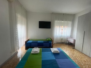 Quarto com duas camas, televisão de tela plana, janela com cortinas e piso de madeira.