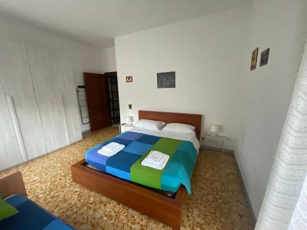 Quarto com cama, cabeceira de madeira, mesa de cabeceira e luminária na parede.