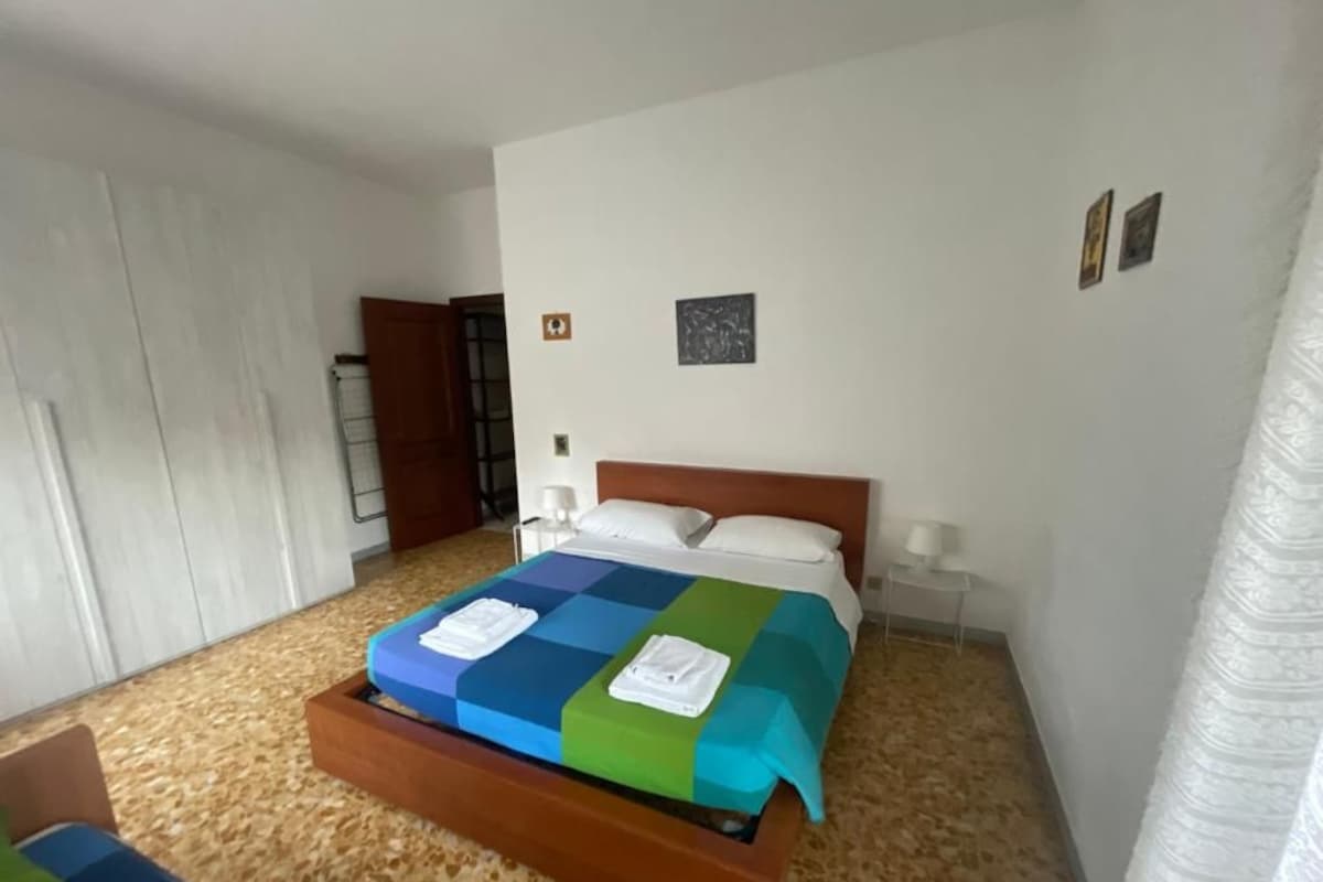 Quarto com cama, cabeceira de madeira, mesa de cabeceira e luminária na parede.