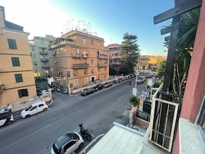 Vista da rua com edifícios, carros estacionados e céu limpo.