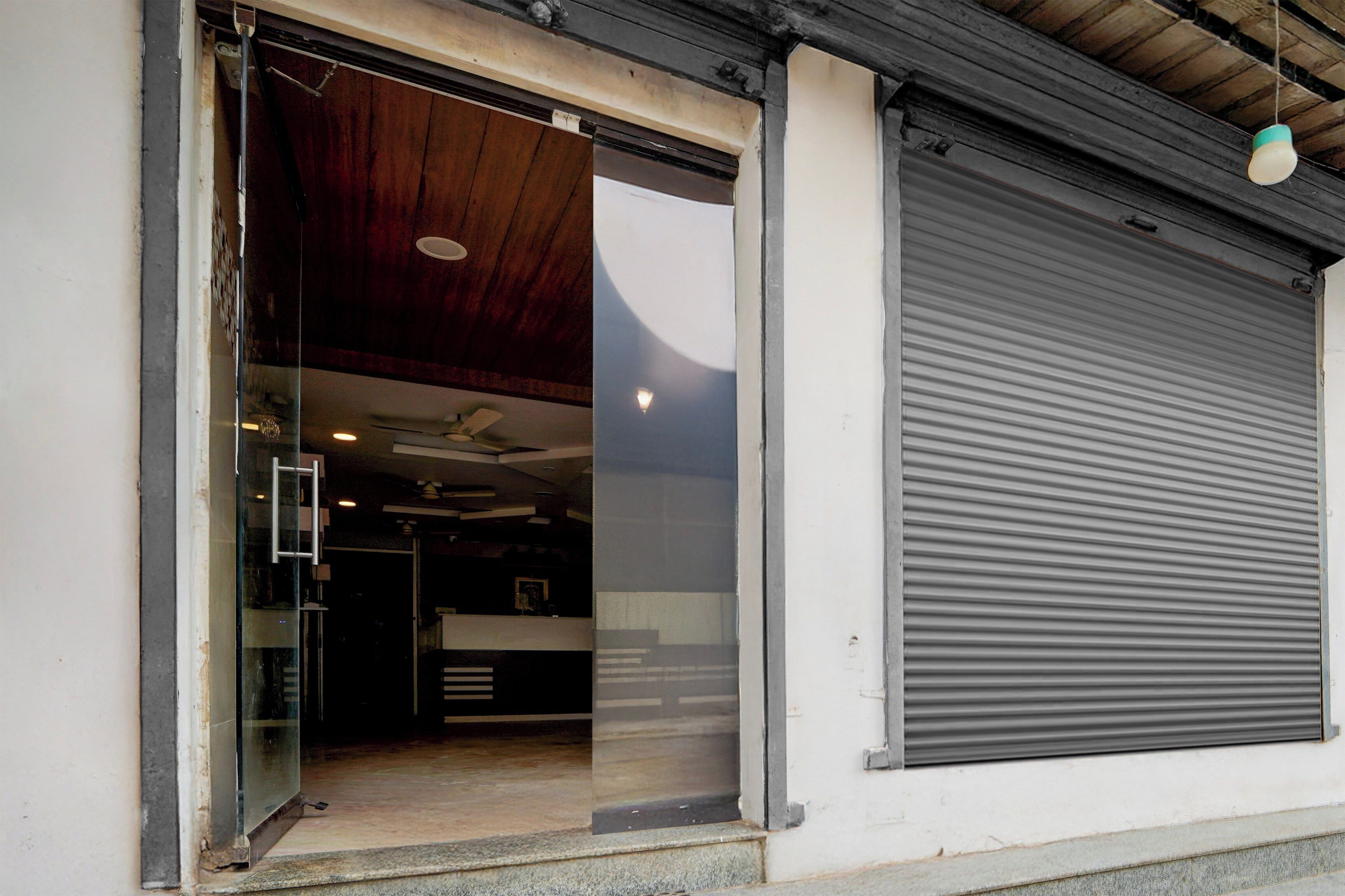 A building entrance with a glass door, a closed roller shutter, and a ceiling fan.