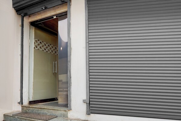 Entrada de un edificio con una persiana metálica bajada y un marco de puerta visible.