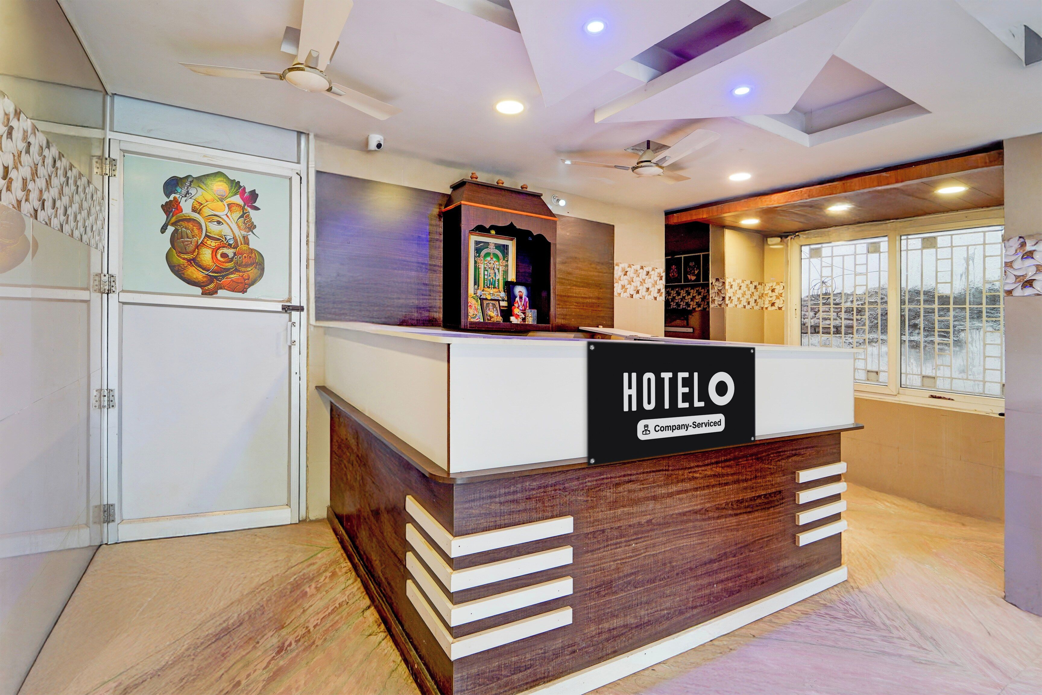 A hotel reception desk with a 'HOTEL' sign, a ceiling fan, and a decorative wall with a floral pattern.