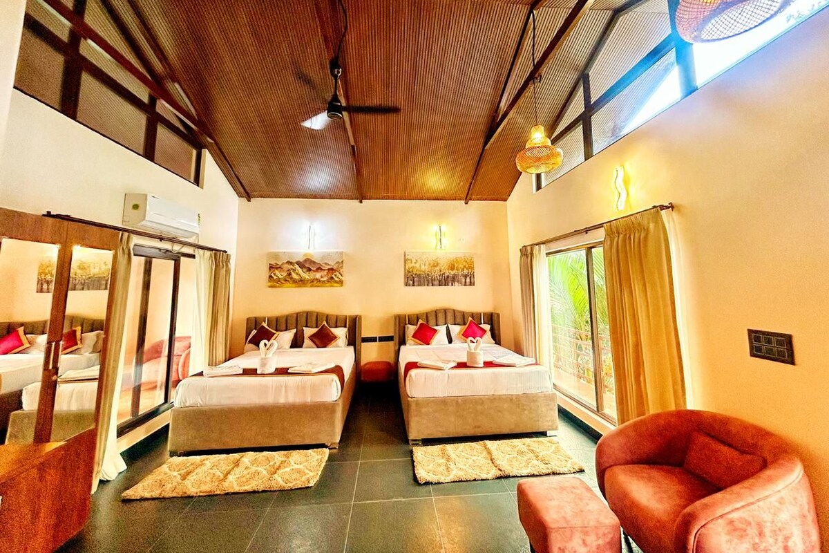 A hotel room with two beds, a ceiling fan, artwork on the walls, and a large window with curtains.
