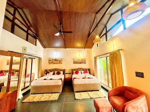 A hotel room with two beds, a ceiling fan, artwork on the walls, and a large window with curtains. - Streamedge Resort (sakleshpur)