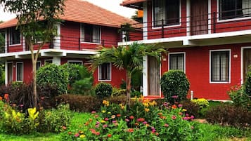 A red building with multiple windows and balconies, surrounded by a well-maintained garden with various plants and flowers.