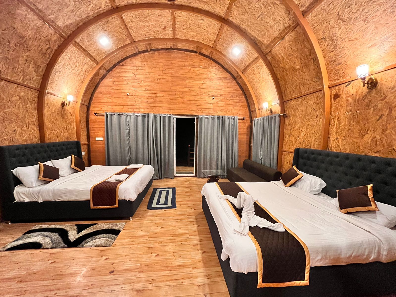 A room with two beds, a wooden ceiling, and a view through a door.