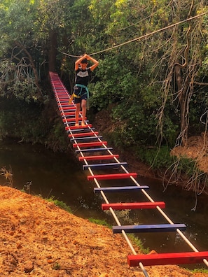 A person walking on a suspended bridge over a river, surrounded by greenery. - Streamedge Resort (Sakleshpur)