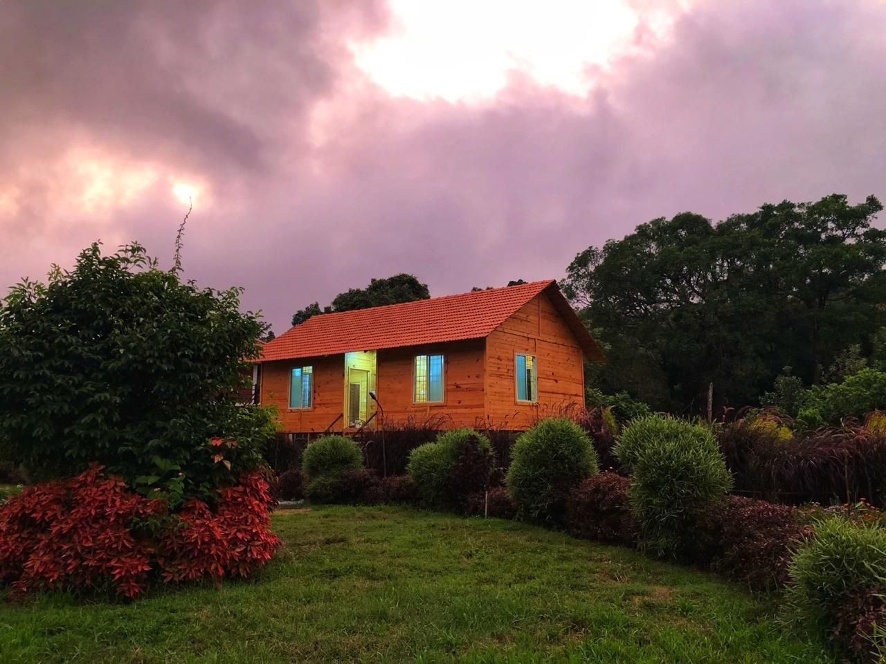 A wooden house with a red roof, surrounded by a well-maintained garden with various shrubs and a lawn.