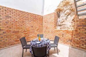 En mur af mursten med et bord dækket til to personer, to stole og en flaske champagne.