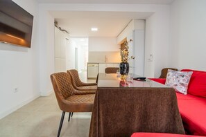 Una sala de estar moderna con un sofá rojo, una mesa de comedor de cristal y dos sillones de cuero marrón.