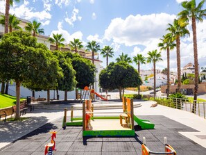 A playground with a slide and climbing structures, surrounded by palm trees and benches. - Cubo's Casa La Roca / urban / air conditioning / terrace / free Wi-Fi (Alhaurín el Grande)