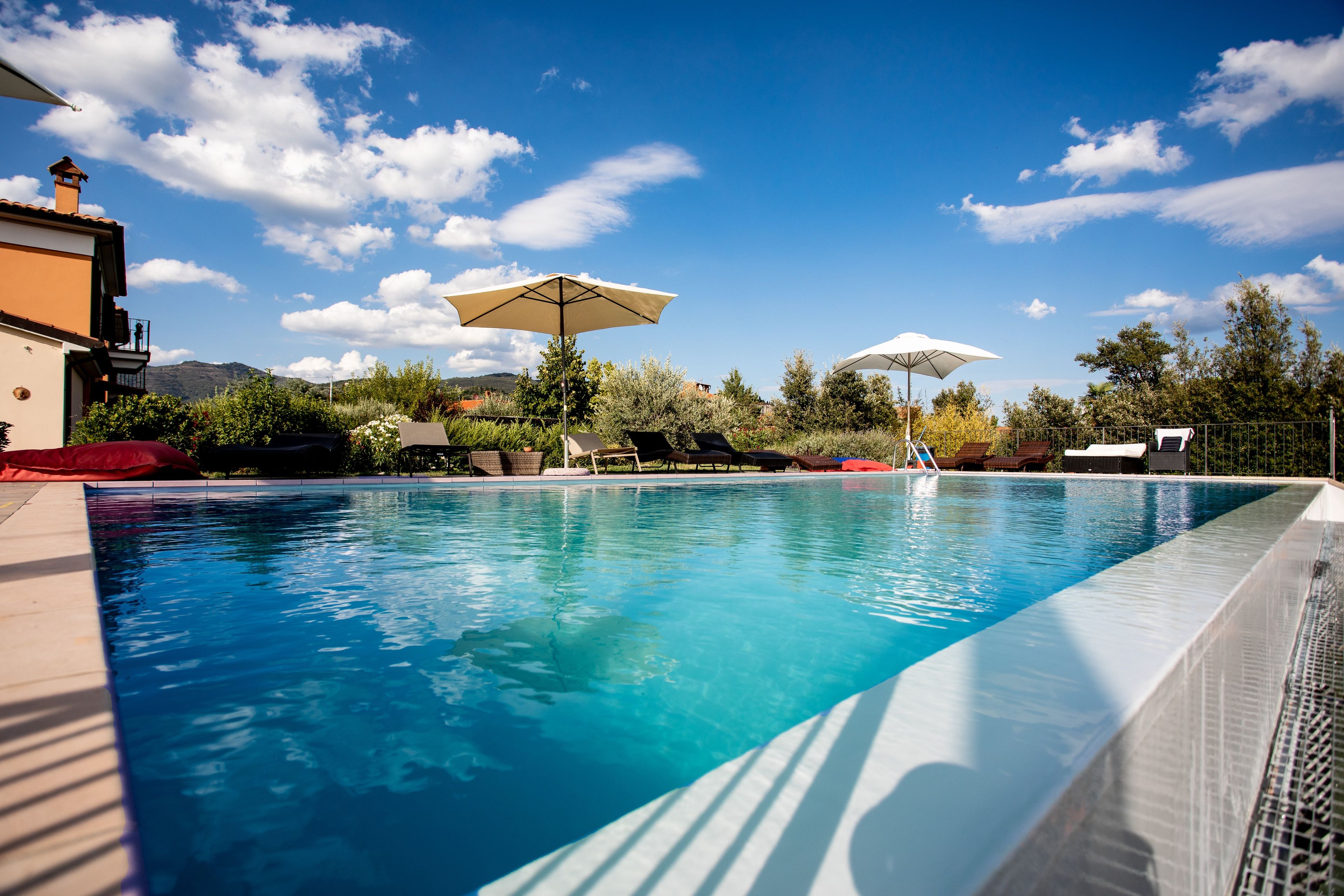 Ein Schwimmbecken mit Liegestühlen und Sonnenschirmen, umgeben von Grünflächen und einem klaren Himmel.