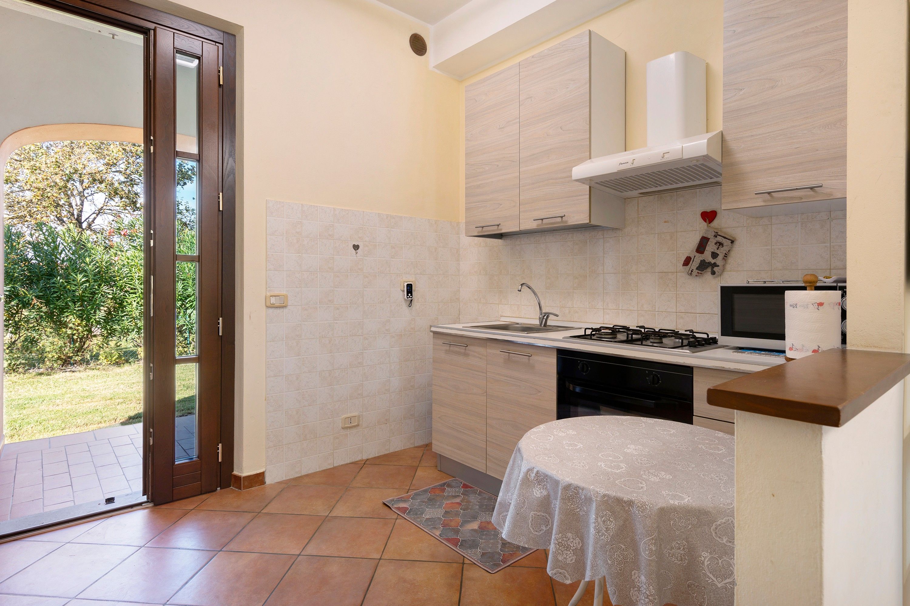 Une cuisine compacte équipée d’une cuisinière à gaz, d’un évier et d’un four à micro-ondes. Une porte-fenêtre coulissante donne accès à un espace patio.
