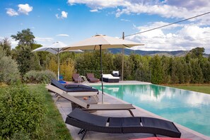 A swimming pool with lounge chairs and umbrellas, surrounded by greenery and mountains in the background.