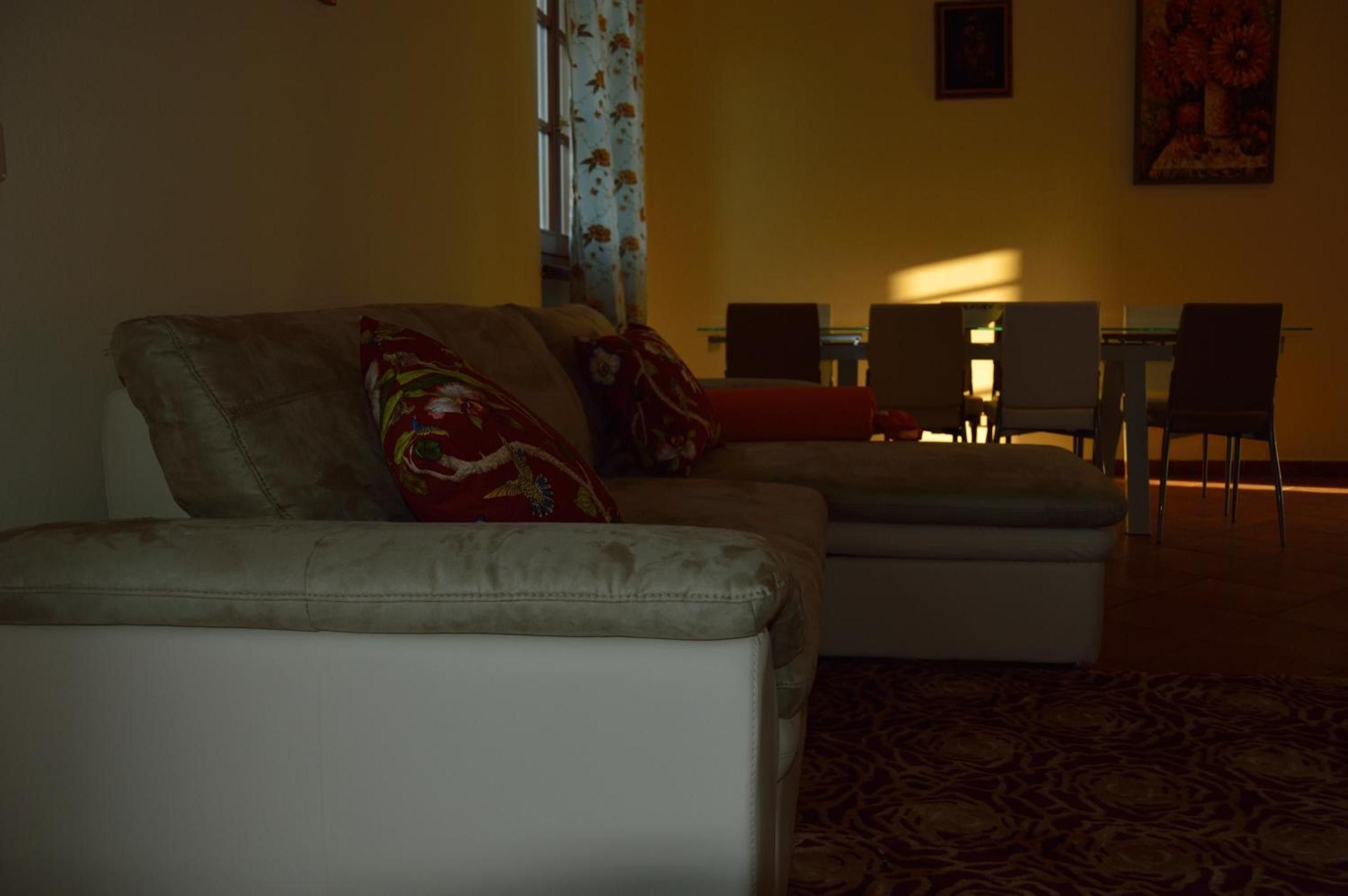Een woonkamer met een bank, poef en een eethoek met stoelen en een tafel.