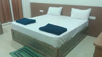 A single bed with white bedding and two folded dark blue blankets.