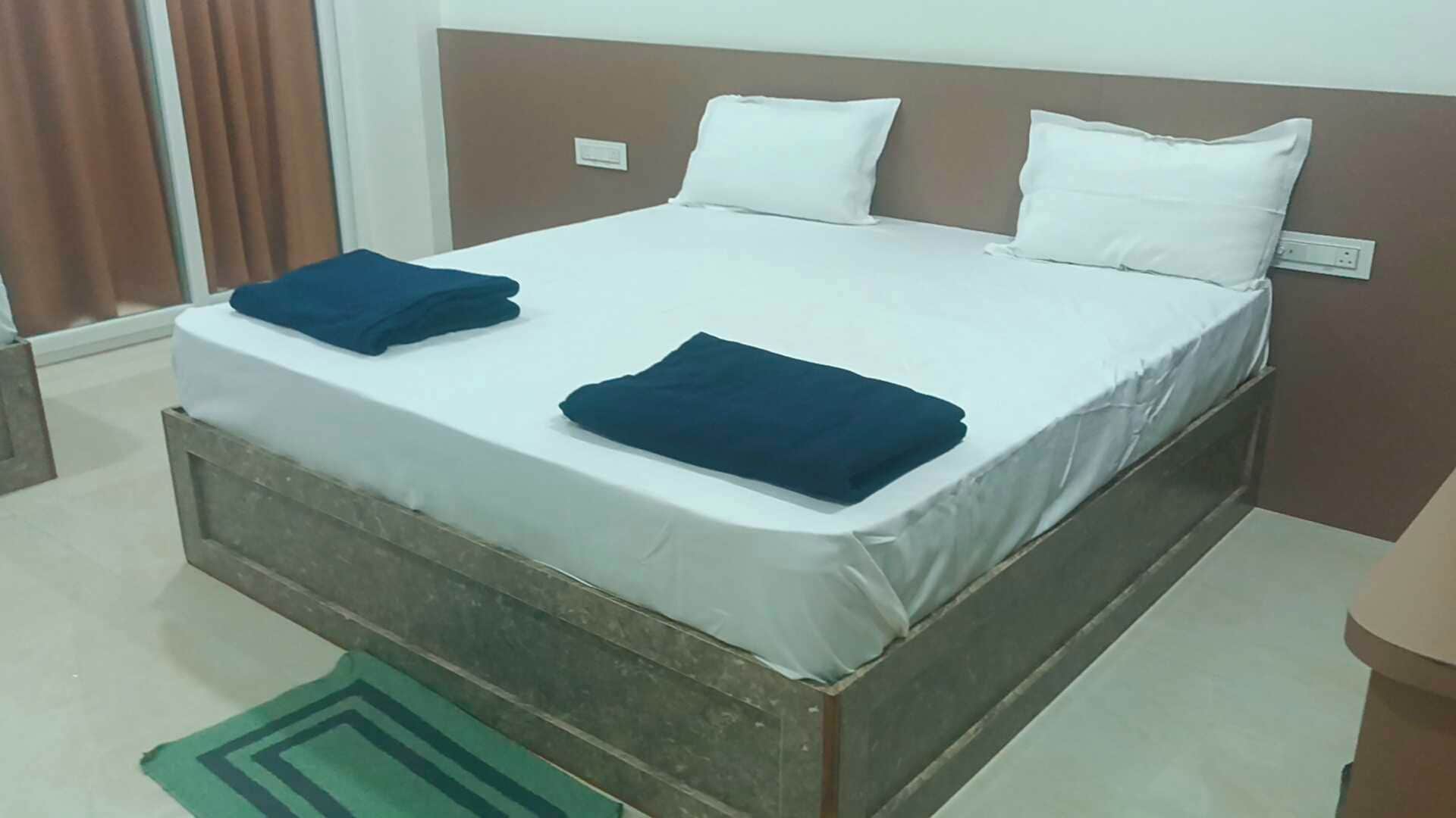 Habitación con cama individual, cabecera de madera, ropa de cama blanca y dos toallas azul oscuro dobladas.