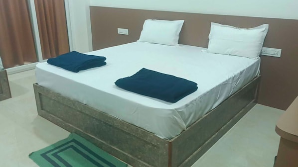 A single-bed room with a wooden headboard, white bedding, and two folded dark blue towels.