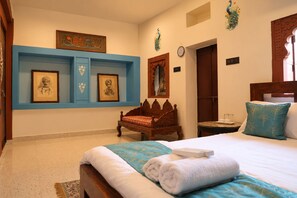 A hotel room with a bed, a wooden chair, a nightstand, and wall-mounted artwork. - Maati Heritage Homestay (Jodhpur)