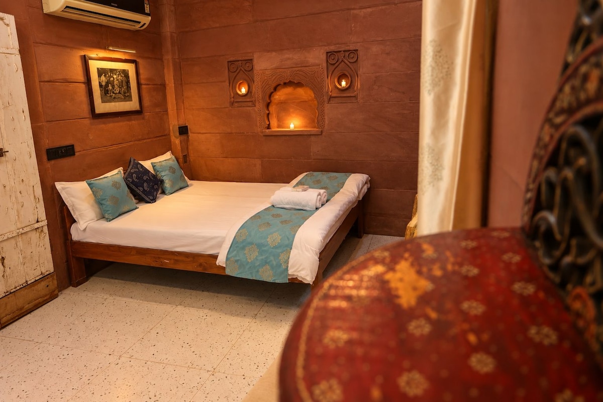 A room with a bed, a framed picture on the wall, and a small alcove with a candle.