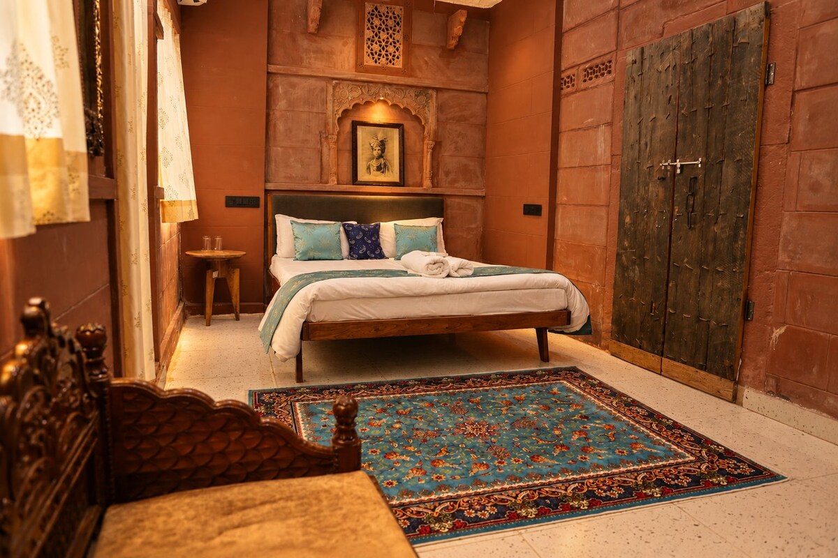 A traditional room with a bed, a wooden wardrobe, a small table, and a decorative rug.
