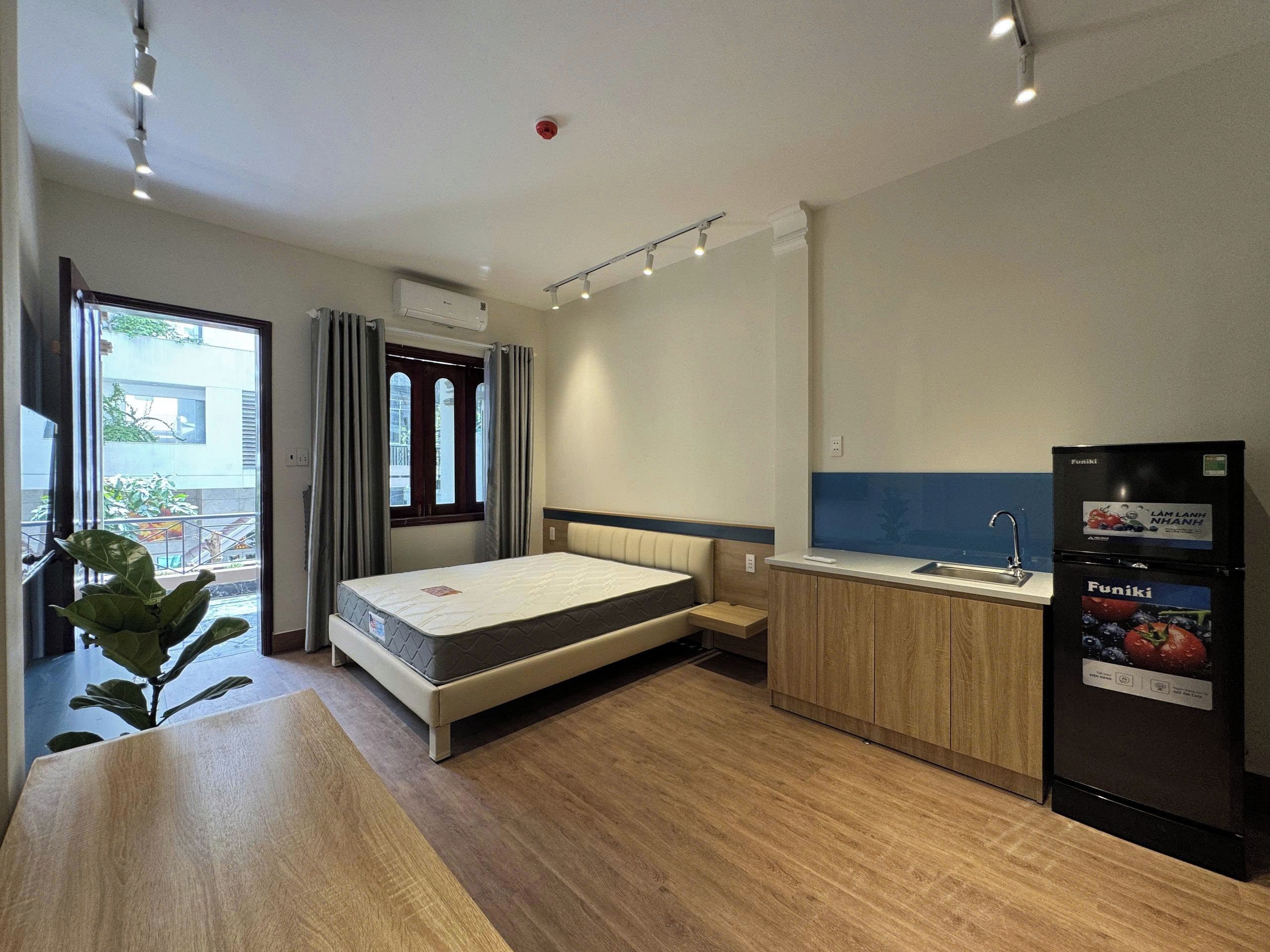 A compact hotel room with a bed, a small kitchenette, and a view through a window.