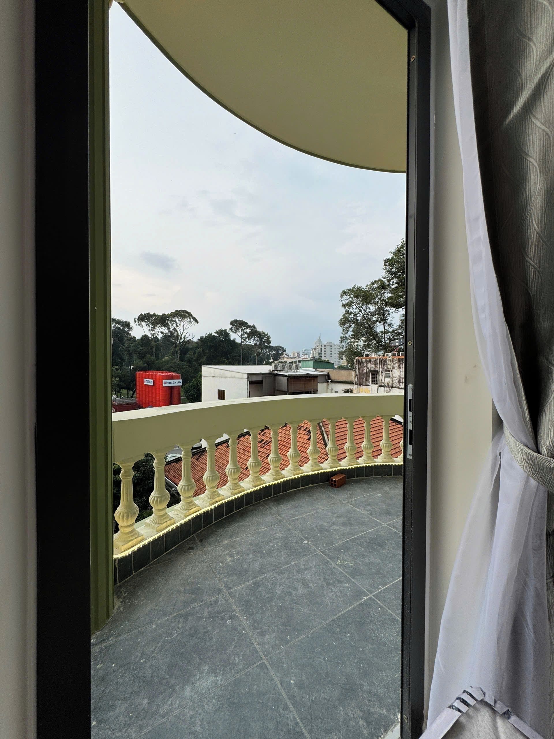 A balcony with a curved railing, a tiled floor, and a view of buildings and trees in the distance.