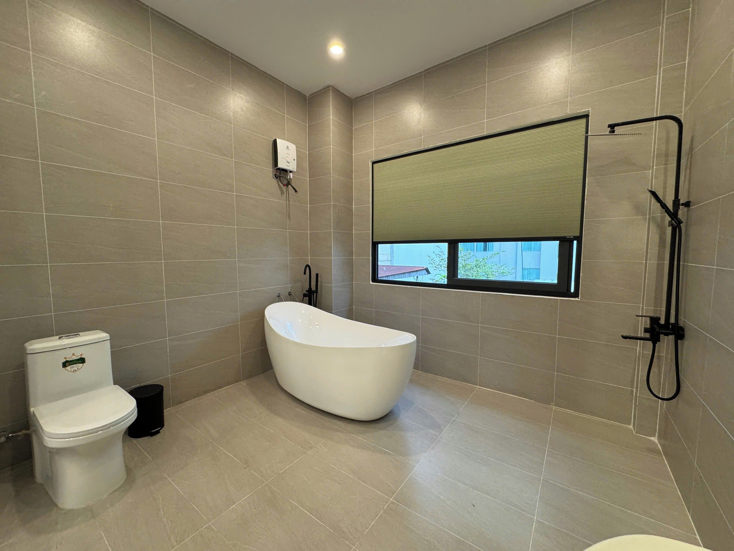 A modern bathroom with a freestanding bathtub, a toilet, and a window with a view.