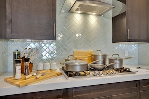 A modern kitchen with a gas stove, pots, and utensils on the counter. - The Reserve | Modern 5BR Henderson Pool Home (Henderson)