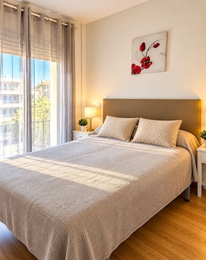 A hotel room with a large bed, a nightstand with a lamp, a wall-mounted artwork, and a view of the outside. - Yamila (Salou)