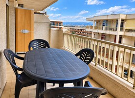 Un balcón con una mesa redonda y cuatro sillas, con vistas a una zona residencial con edificios y cielo despejado.