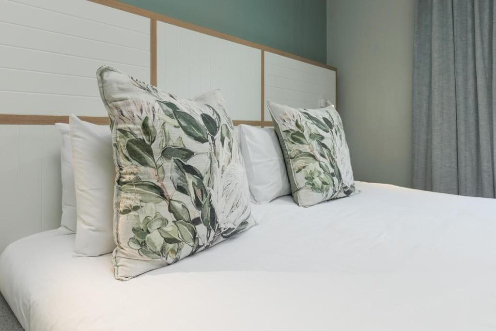 Una cama con ropa blanca y dos almohadas estampadas con motivos florales.