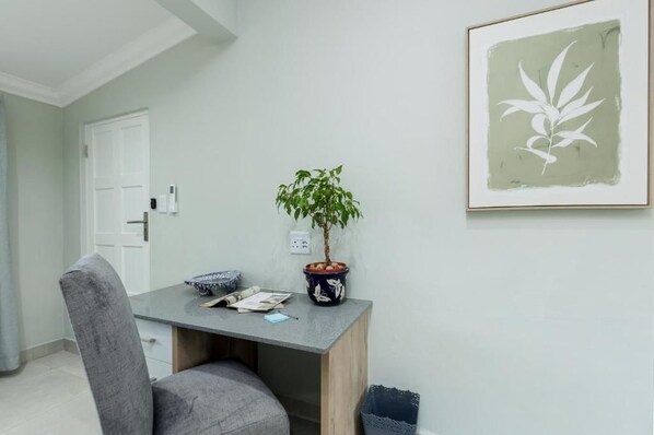 A room with a desk, chair, potted plant, framed artwork, and a door.