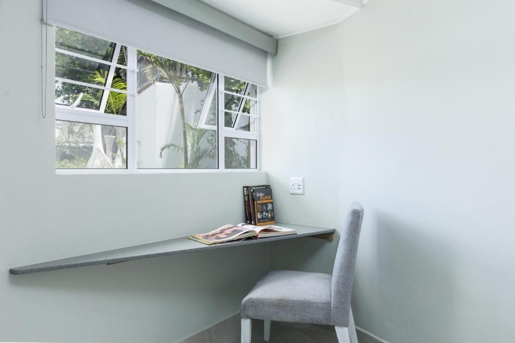 A corner room with a window, a grey chair, and a shelf with books.
