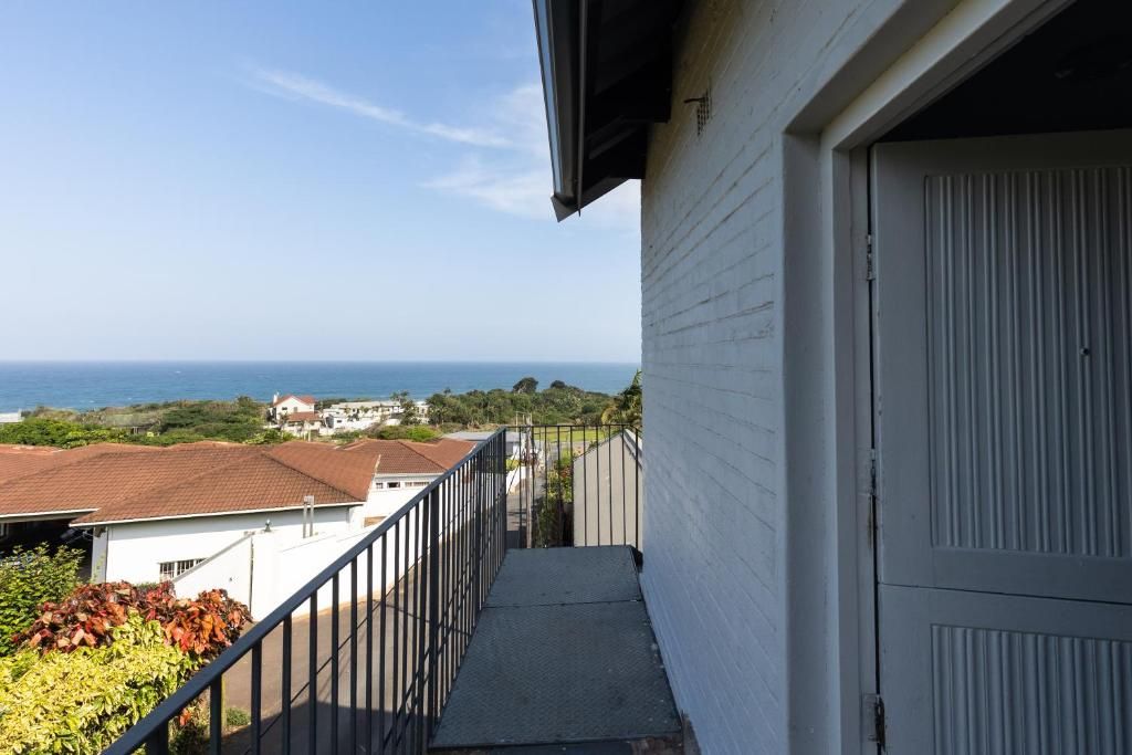 A balcony with a view of the sea, a white building, and a metal railing.