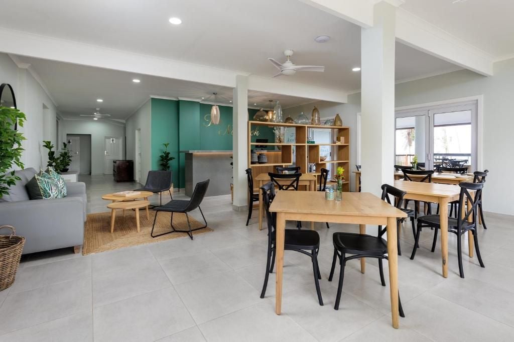Un vaste espace de vie comprenant une table à manger, des chaises et un canapé. On y trouve également une bibliothèque avec des objets décoratifs et un ventilateur de plafond.