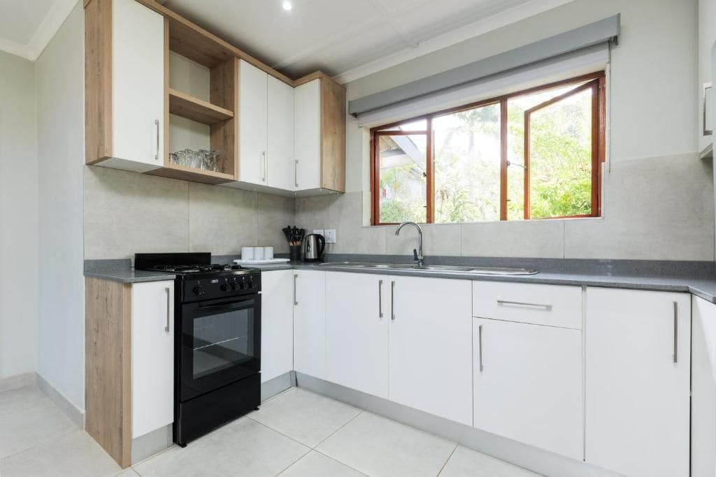 Una cocina moderna con armarios blancos, una estufa negra y un ventanal que proporciona luz natural.