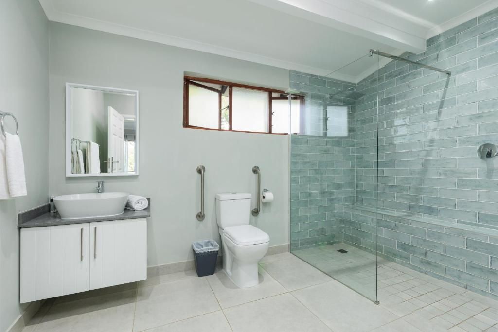 A bathroom with a white sink, a toilet, a glass shower enclosure, and a mirror.