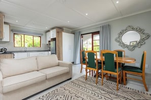 A modern living room with a sofa, dining table, chairs, and a patterned rug.