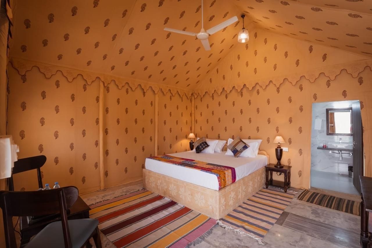 Ein Hotelzimmer mit Bett, Deckenventilator, Nachttisch, Stuhl und einem durchgehenden Türspalt sichtbarem Badezimmer.