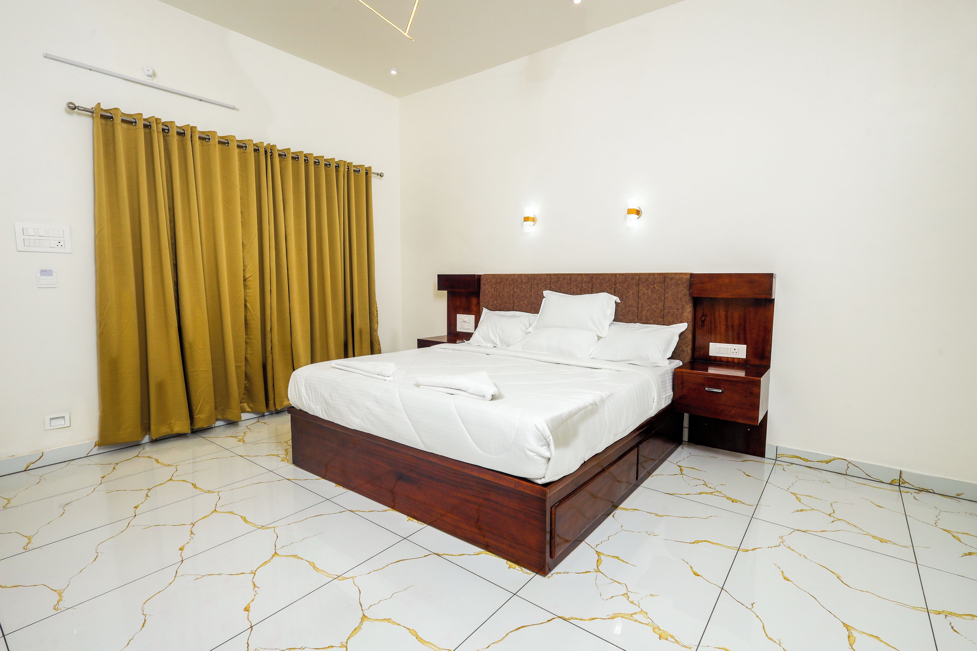 Quarto de hotel com uma cama grande, mesas de cabeceira, painel de cabeceira de madeira e uma cortina.