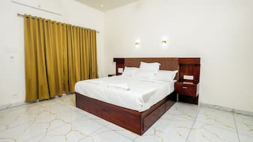 Quarto de hotel com uma cama grande, mesas de cabeceira, painel de cabeceira de madeira e uma cortina.