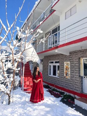 Un edificio de dos pisos con fachada roja y blanca, un balcón y suelo cubierto de nieve.
