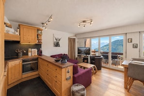 Una cucina moderna con mobili in legno, una zona pranzo con tavolo e sedie, e un soggiorno con divano e camino.