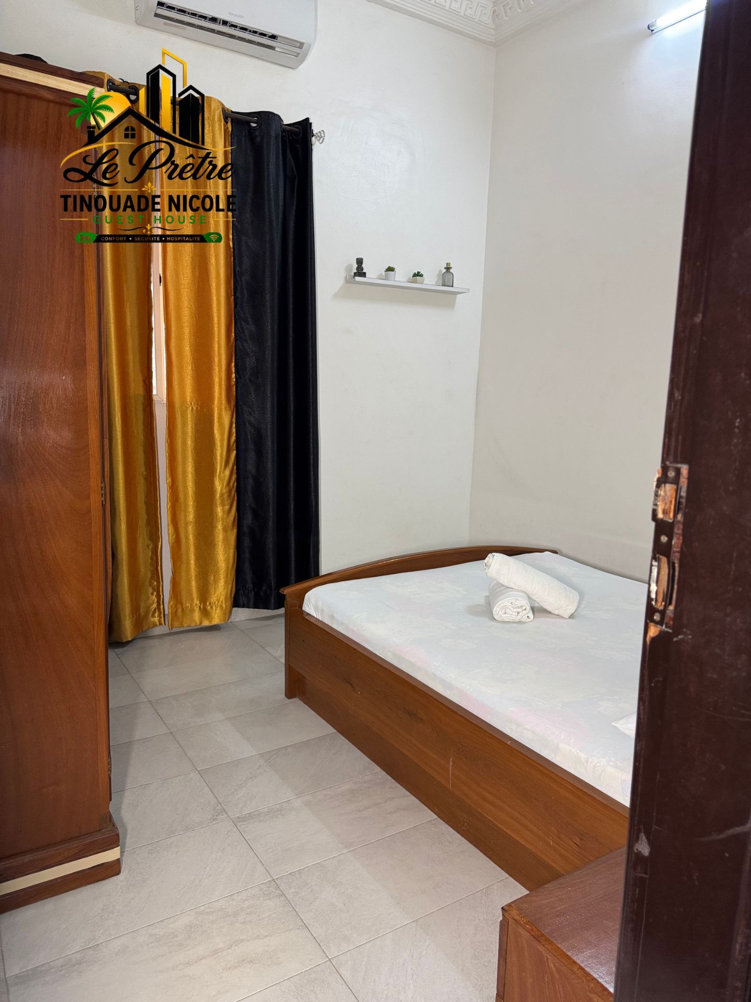 A hotel room with a bed, a wardrobe, a shelf with decorative items, and a curtain.