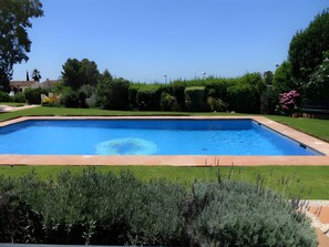 A rectangular swimming pool with a clear blue water surface, surrounded by a well-maintained lawn and various shrubs. - Apartment 'Residencia La Fuente' with Shared Pool, Wi-Fi and Air Conditioning (Mijas)